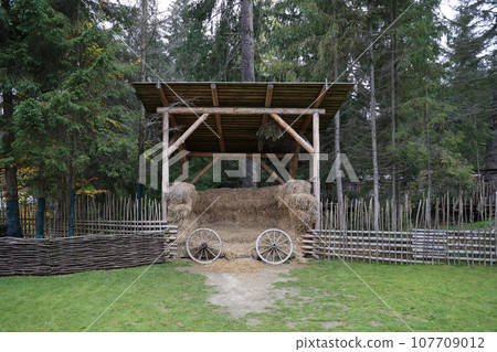 Place with stacks of hay cubes and rustic wooden wheels of old cart 107709012
