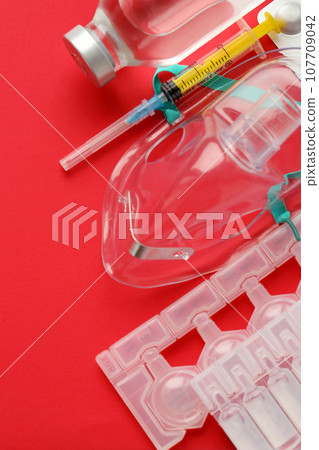 Coronavirus treatment concept. A medical face mask nebulizer for treatment of respiratory tract and packs of ampoules flat layed on red background 107709042
