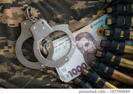Ukrainian army machine gun belt shells and handcuffs on military uniform. Concept of bribery and war crimes 107709094