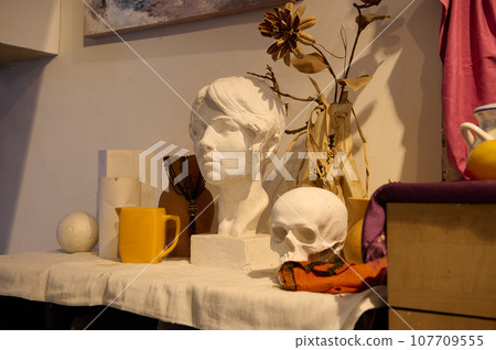 Close-up. Plaster figure and heads, skeleton and objects for drawing, displayed on a table in creative art studio 107709555
