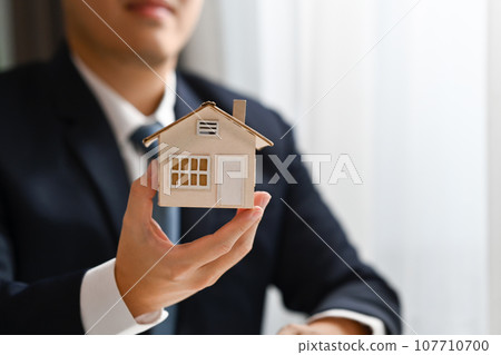 Close up shot of male realtor hand holding house model. Real estate, loan and property investment concept 107710700
