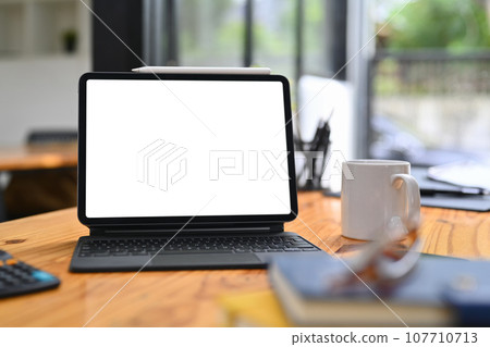 Wooden office desk with digital tablet, pencil holder and coffee cup. Blank screen for your advertising text message 107710713