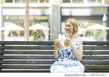 Woman sitting on a bench and drinking iced coffee Woman sitting on a bench and drinking iced coffee 107712117