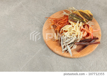 Different types of dried fish and squid on a round wooden board. Beer snack. Snack for men's company. Different types of dried fish and squid on a round wooden board. Beer snack. Snack for men's company. 107712355