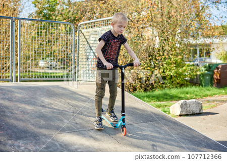 Child on kick scooter in park. Kids learn to skate roller board. Little boy skating on sunny summer day. Outdoor activity for children on safe residential street. Active sport for preschool kid. boy Child on kick scooter in park. Kids learn to skate roller board. Little boy skating on sunny summer day. Outdoor activity for children on safe residential street. Active sport for preschool kid. boy 107712366
