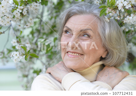 Close-up portrait of smiling elderly woman posing in summer park 107712431