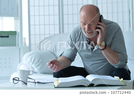 old man with book talking on phone and taking notes old man with book talking on phone and taking notes 107712440