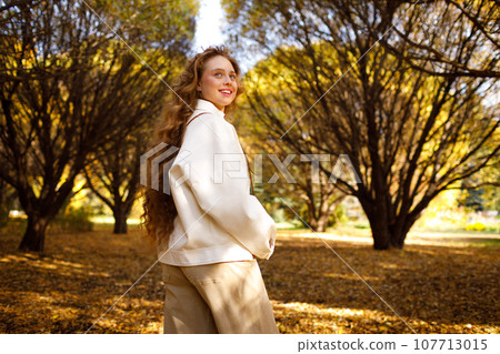 Smiling young woman with the photo camera walking in the park 107713015