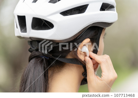 Young woman wearing a cycling helmet and earphones 107713468