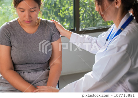 Overweight woman having consultation doctor at the clinic. portrait of friendly smiling doctor putting hand on shoulder supporting patient, giving consultation during medical examination in clinic 107713981