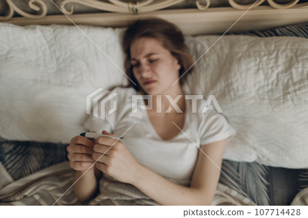 Young woman has flu catarrh ill sick disease treatment cold check measures temperature thermometer lay in bed Young woman has flu catarrh ill sick disease treatment cold check measures temperature thermometer lay in bed 107714428