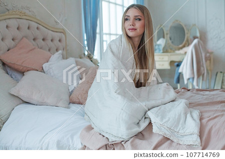 Happy young woman with long blonde hair sitting in bed in the morning 107714769