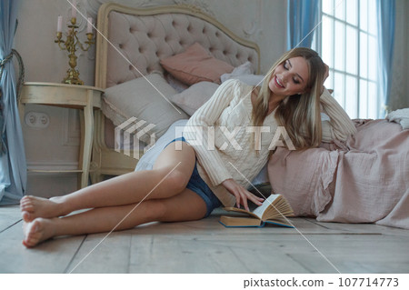 Pretty young woman enjoying reading a book at home smiling in pleasure 107714773