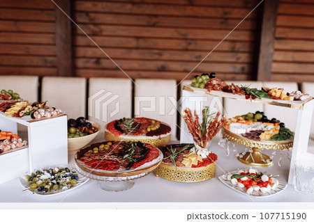 Appetizers table with meat and cheese. Salami, sausages, variation of cheese, grapes, tomatoes, green olives, rosemary, tapas on wooden plates. Snack finger food meal for wine, starter. 107715190