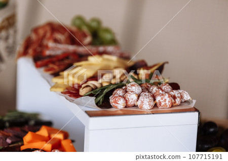 Appetizers table with meat and cheese. Salami, sausages, variation of cheese, grapes, tomatoes, green olives, rosemary, tapas on wooden plates. Snack finger food meal for wine, starter. 107715191
