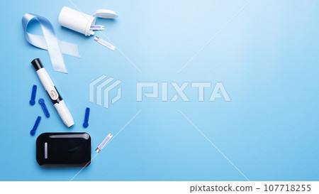 Diabetes awareness concept of ribbon glucose meter test strips and lancets on blue background flat lay Diabetes awareness concept of ribbon glucose meter test strips and lancets on blue background flat lay 107718255