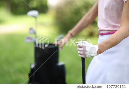 Female hand of golfer in glove holds bag with golf clubs 107720151