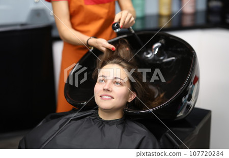 Master washes her hair in sink for client in hairdressing salon 107720284