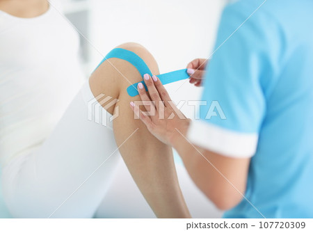 Doctor glues kinesio tape to patient's knee Doctor glues kinesio tape to patient's knee 107720309