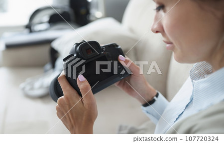 Woman holds black professional camera in her hands Woman holds black professional camera in her hands 107720324