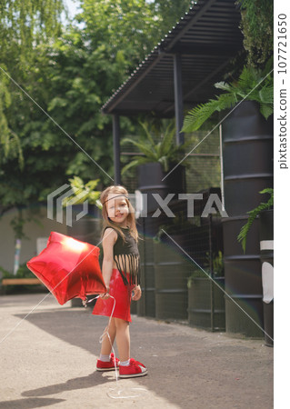 Girl in a red leather skirt walks with an balloon foil star-shaped on birthday Girl in a red leather skirt walks with an balloon foil star-shaped on birthday 107721650