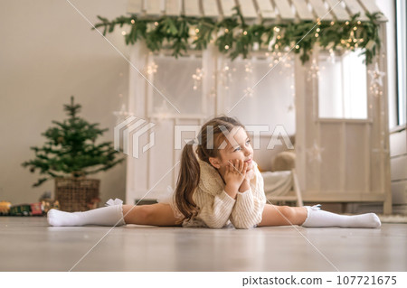 A thoughtful gymnast girl is sitting in a twine pose in a room decorated for the new year and looks away 107721675