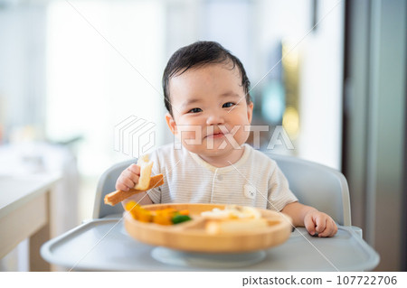 A 9-month-old baby who is in a good mood after grabbing and eating in the late stage of baby food 107722706