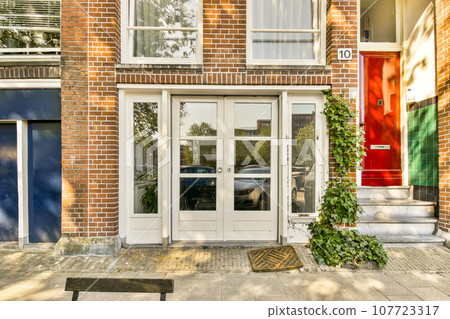 a brick building with a white door and green plants growing on the sidewalk in front of the entrance to the building 107723317
