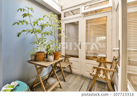 a balcony with some plants on the table and two wooden folding chairs in front of the door to the room 107723318