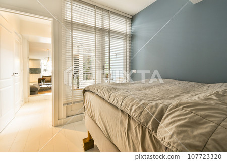 a bedroom with blue walls and white shutters on the window behind it is a bed that has a beige comforter a bedroom with blue walls and white shutters on the window behind it is a bed that has a beige comforter 107723320