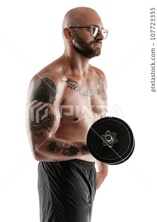 Athletic bald, tattooed man in black shorts is posing with a dumbbell isolated on white background. Close-up portrait. 107723355
