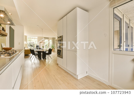 a kitchen and dining area in a house with wood flooring, white cabinets and an open door leading to the living room a kitchen and dining area in a house with wood flooring, white cabinets and an open door leading to the living room 107723943