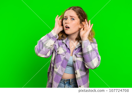 Young woman trying hear you looking confused and frowning, keeping arm near ear for louder voice 107724708