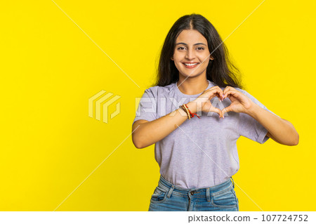Smiling pretty woman makes heart gesture demonstrates love sign expresses good feelings and sympathy Smiling pretty woman makes heart gesture demonstrates love sign expresses good feelings and sympathy 107724752