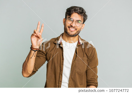 Happy smiling Indian young man showing victory sign, hoping for success and win, doing peace gesture 107724772