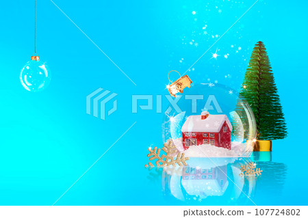Christmas blue background with transparent snow globe, inside with house and Christmas tree. New Year background, winter composition from glass ball Christmas blue background with transparent snow globe, inside with house and Christmas tree. New Year background, winter composition from glass ball 107724802
