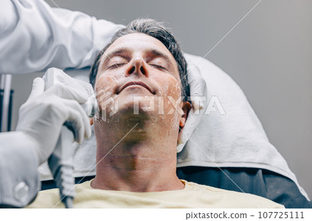 Skin doctor using HIFU resurfacing facial skincare treatment technology with adult male to reduce wrinkles and scars at anti aging clinic 107725111