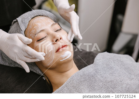 Woman facial massage face skin treatment with natural essence herbal extract moisturising cream in beauty spa clinic. Woman facial massage face skin treatment with natural essence herbal extract moisturising cream in beauty spa clinic. 107725124