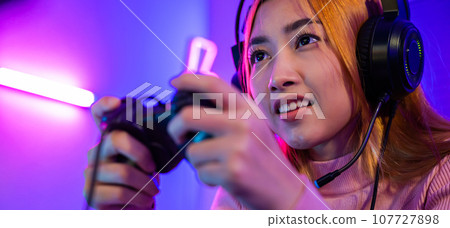 You win. Gamer using joystick controller plays online video game with computer neon lights she winning, woman wear gaming headphones playing live stream esports games console at home celebrating win You win. Gamer using joystick controller plays online video game with computer neon lights she winning, woman wear gaming headphones playing live stream esports games console at home celebrating win 107727898