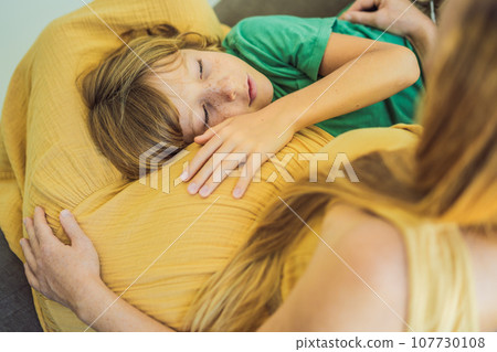 A heartwarming moment: pregnant mother and her older son sit on the sofa, engaging in a tender conversation about the upcoming pregnancy 107730108