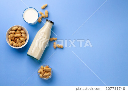 Peanut non dairy milk in glass bottle with bowl of peanuts on blue background 107731748