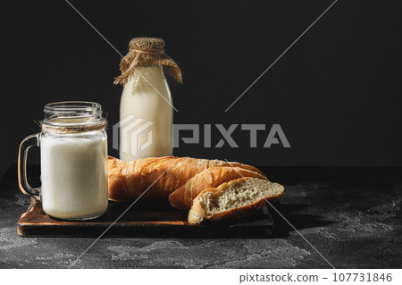 Glass of milk with sliced baguette on wooden board Glass of milk with sliced baguette on wooden board 107731846