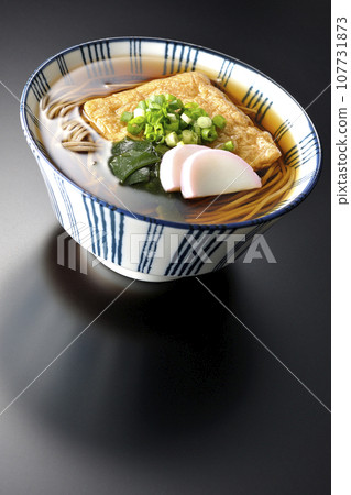 Kitsune 蕎麥麵配上炸豆腐、魚糕、裙帶菜和蔥,在黑色背景下拍攝 Kitsune 蕎麥麵配上炸豆腐、魚糕、裙帶菜和蔥,在黑色背景下拍攝 107731873