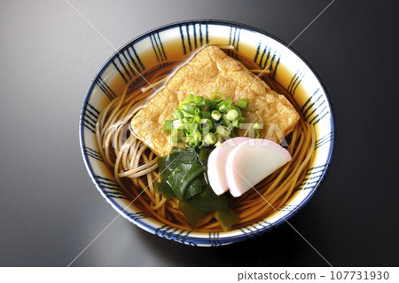 黑色背景下的狐狸蕎麥麵,上面放著炸豆腐、魚板、裙帶菜和蔥 黑色背景下的狐狸蕎麥麵,上面放著炸豆腐、魚板、裙帶菜和蔥 107731930