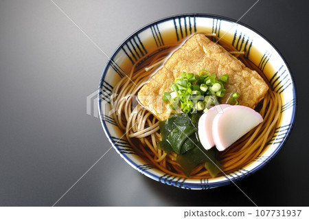 An overhead shot of fox soba noodles topped with fried tofu, kamaboko, wakame, and green onions against a black background An overhead shot of fox soba noodles topped with fried tofu, kamaboko, wakame, and green onions against a black background 107731937