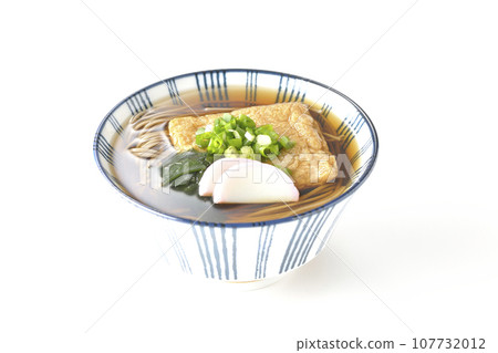 Kitsune 蕎麥麵上面放著炸豆腐、魚糕、裙帶菜和蔥，在白色背景下拍攝 107732012