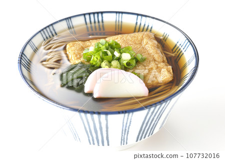 Kitsune 蕎麥麵上面放著炸豆腐、魚糕、裙帶菜和蔥，在白色背景下拍攝 107732016