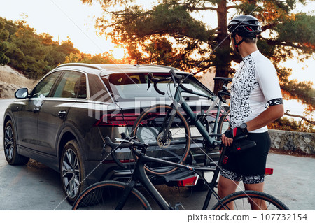 Male cyclist loading his bicycle on a rack of his crossover car Male cyclist loading his bicycle on a rack of his crossover car 107732154