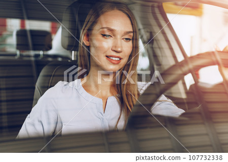 Attractive young woman sitting in new car in showroom Attractive young woman sitting in new car in showroom 107732338