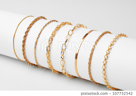 Set of golden bracelets on display on white background 107732542